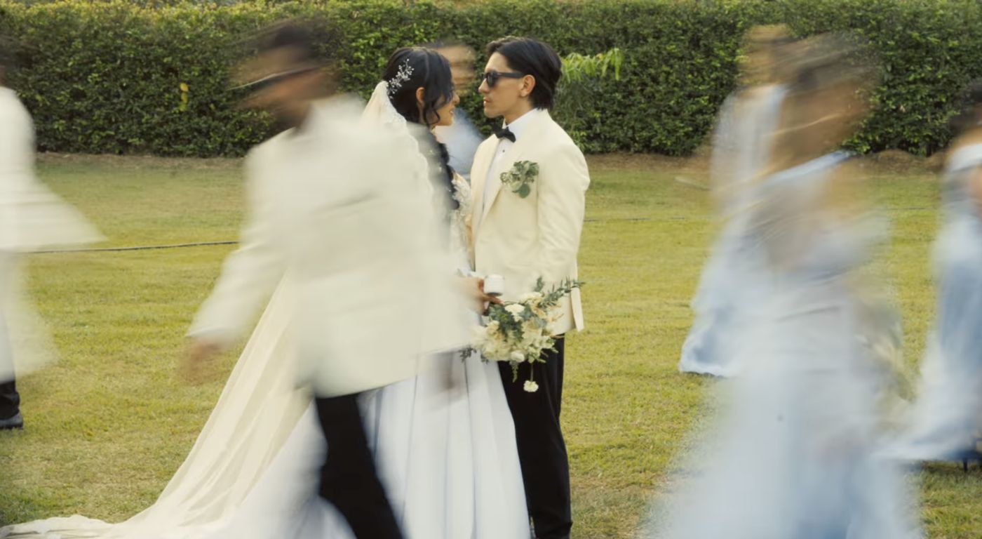 Paola y Andres de frente en el jardín mientras los invitados pasan en movimiento