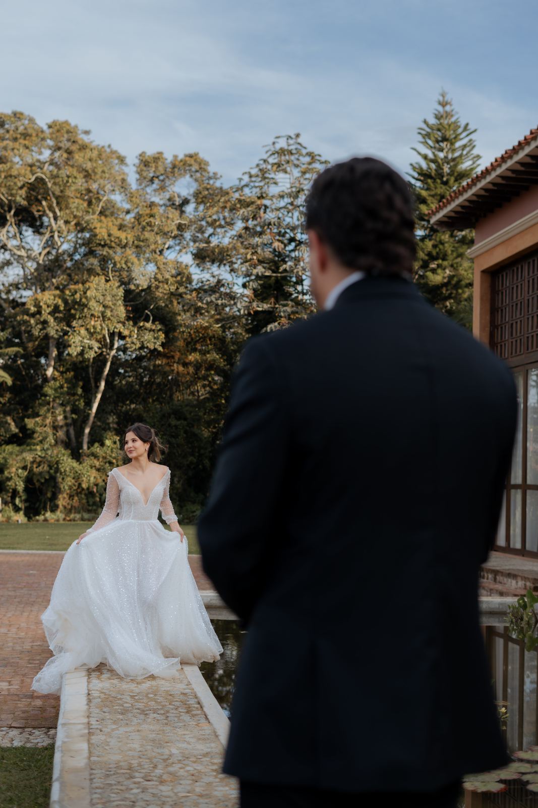 Novia caminando por un borde de piedra con el novio desenfocado en primer plano