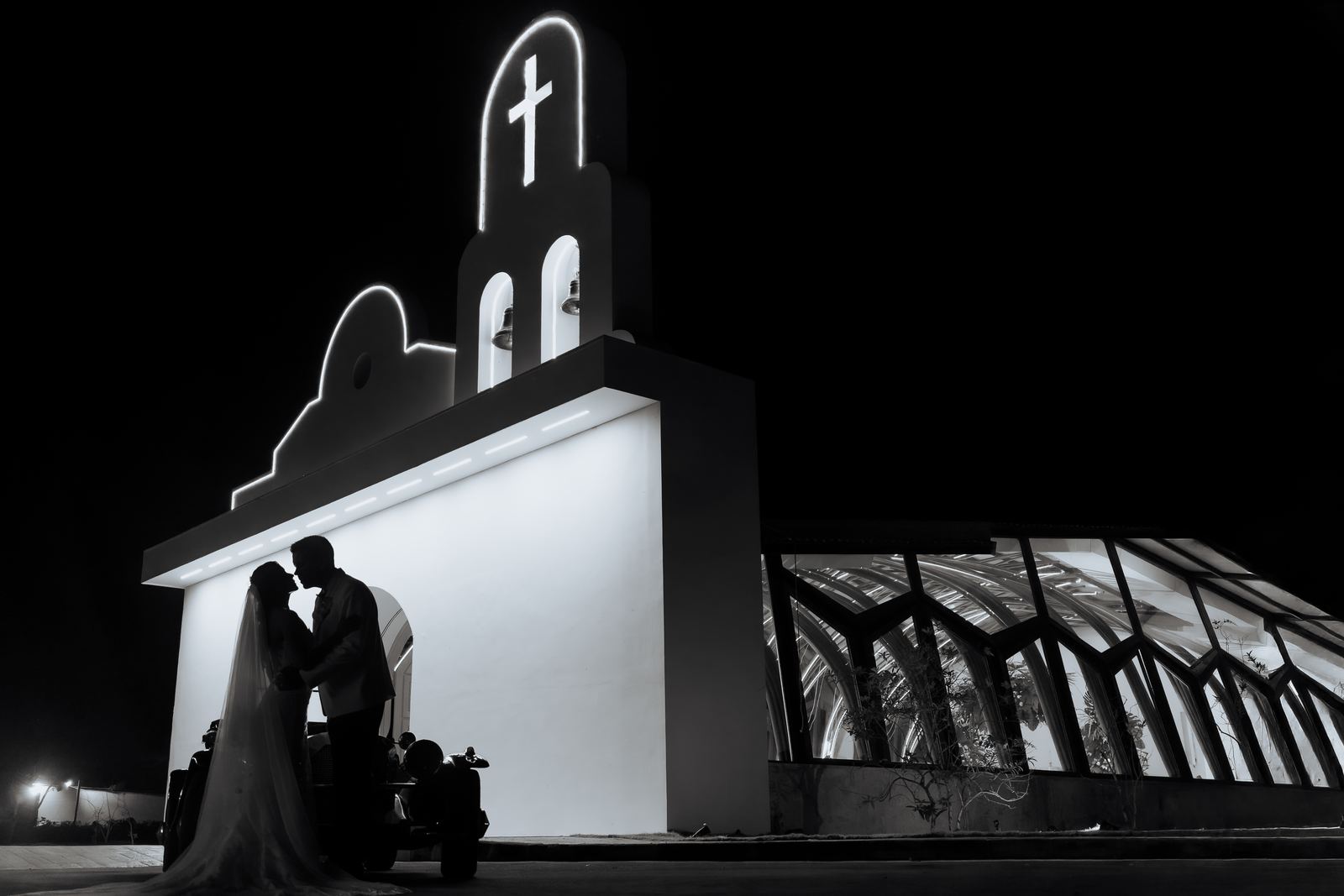 Silueta de los novios besándose frente a una capilla iluminada de noche, en blanco y negro