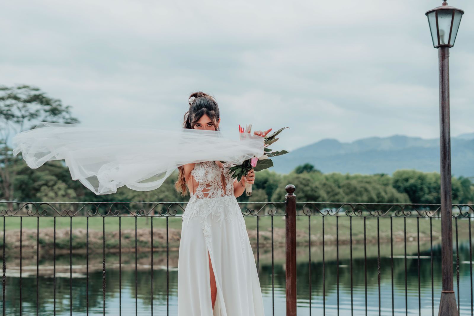 Novia con el velo al viento frente a una laguna y las montañas